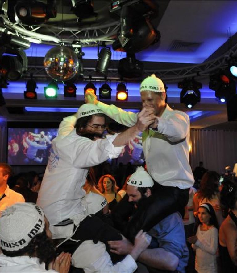 אנשי צוות "נחמנים משמחים" מרימים את החתן על הכתפיים באירוע שמח עם ריקודים אנרגטיים ותאורה חגיגית.